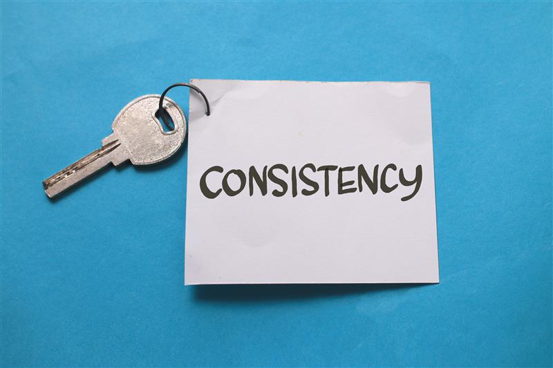 Key attached to a white note with the word “Consistency” written on it, set against a blue background, symbolising the importance of consistent branding and marketing.